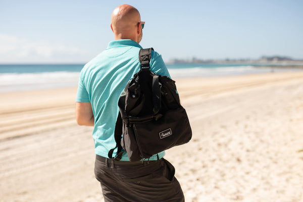 Black recycled tote bag worn as backpack on man at beach, showing front pocket and shoulder straps