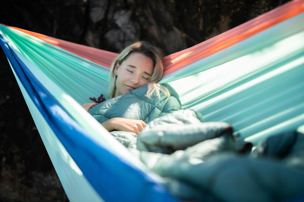 Woman relaxing in colorful recycled hammock with attached puffy blanket combo in sage green and rainbow stripes.