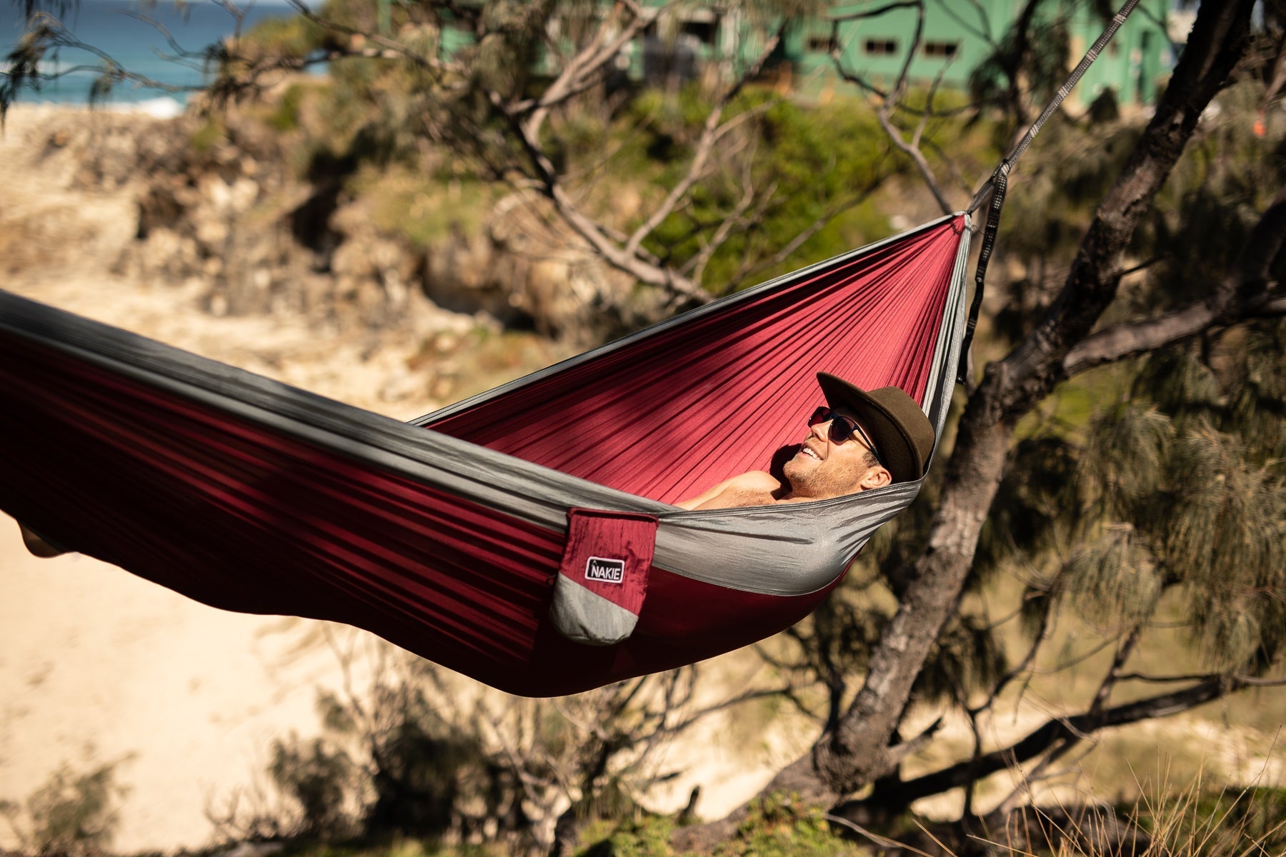 Person relaxing in a Nakie Merlot Red hammock in a forest.