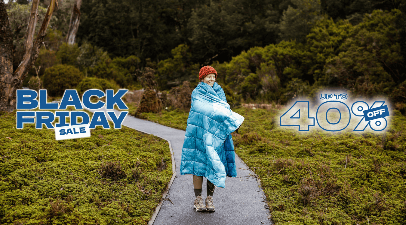 Two people wrapped in a blue puffy blanket sitting on a mountain edge