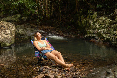Woman relaxing in the Kasey Rainbow Camping Chair at a rainforest creek