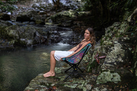 Woman leaning back in the Kasey Rainbow Camping Chair on a creek rock