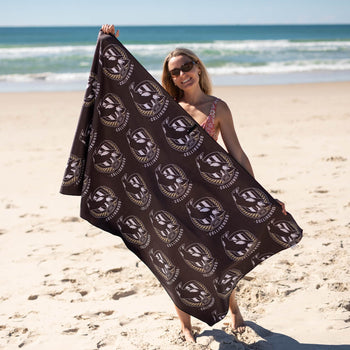 Black Collingwood Magpies AFL beach towel with white and gold logo print, held up on sandy beach