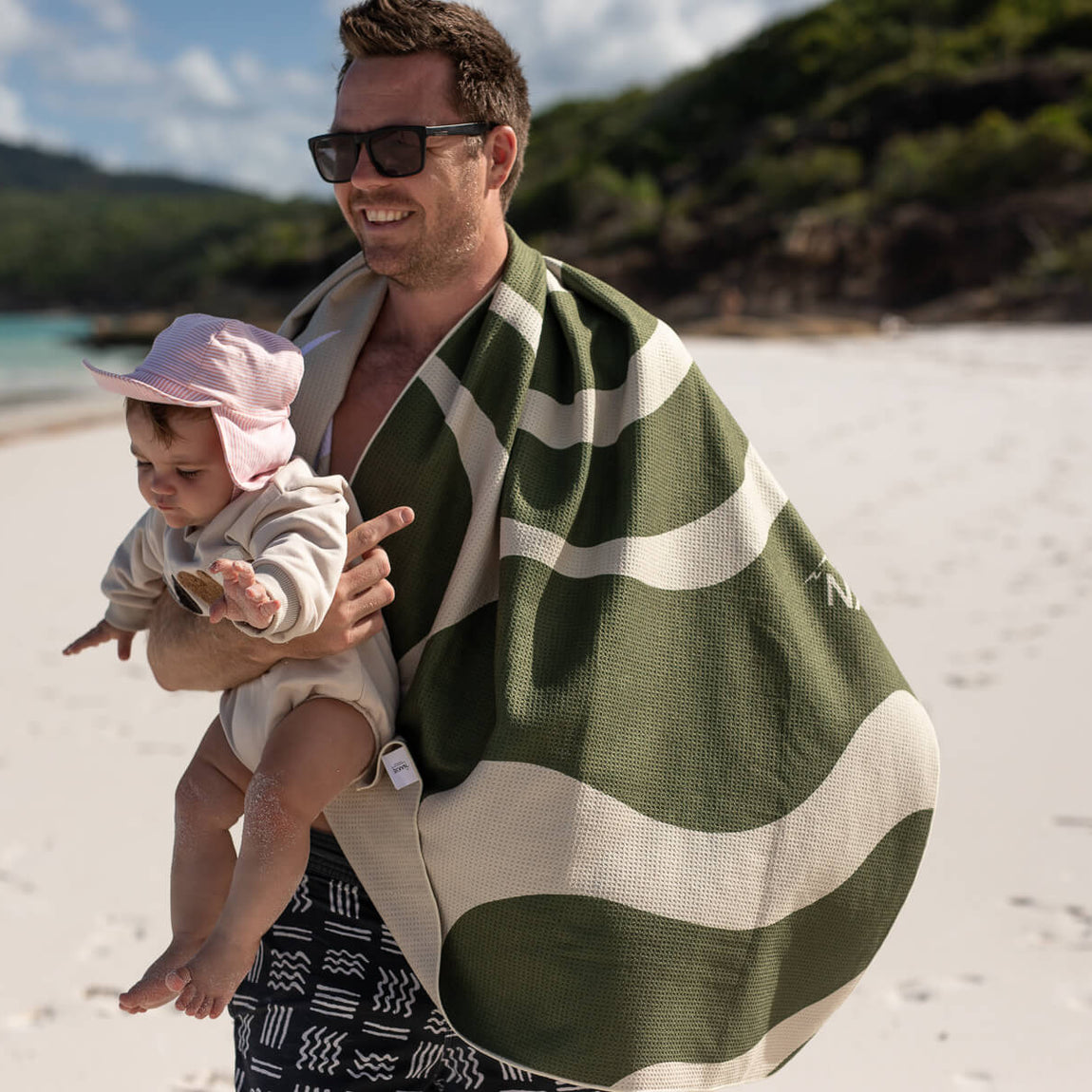Eucalyptus green and cream striped recycled beach towel draped over man's shoulder at beach