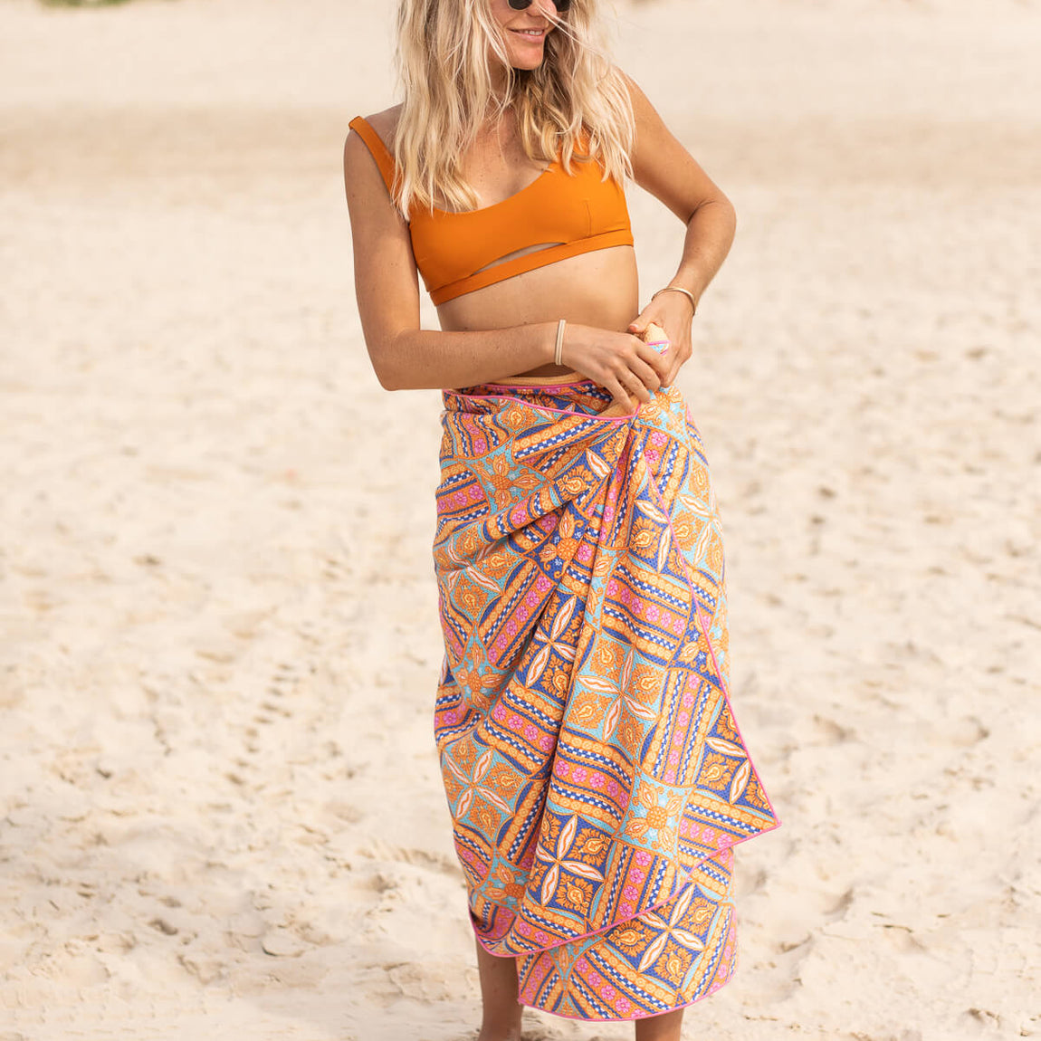 Multicoloured geometric patterned beach towel wrapped around woman's waist on sand.