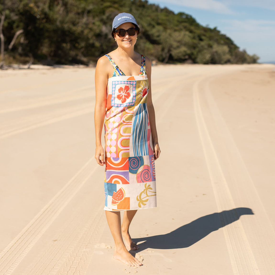 Colorful patchwork beach towel worn as dress on sand, featuring retro floral and geometric patterns in orange, blue
