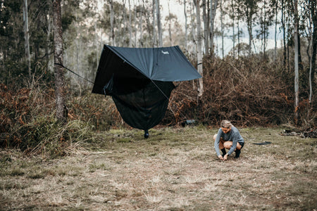 Woman setting up a Nakie ultralight no knot tarp at a campsite, demonstrating easy assembly and portability for outdoor adventures.