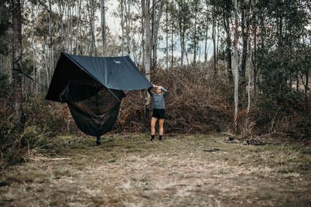 Woman effortlessly setting up a Nakie ultralight no knot tarp at a campsite, showcasing the ease of assembly and the versatility of our eco-friendly outdoor gear.