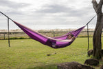 A calming image of a purple Nakie hammock elegantly stretched between two trees, providing a sustainable oasis for rest and rejuvenation preview #6