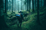 Image of a man walking in a campsite with Nakie's Deep Ocean Blue Sustainable Down Puffy Blanket attached to his backpack, ready for outdoor adventures with sustainable warmth. preview #8