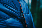 Close-up photo of unopened Nakie's Deep Ocean Blue Sustainable Down Puffy Blanket, showcasing its compact and portable design for outdoor enthusiasts. preview #10