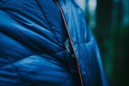 Close-up photo of unopened Nakie's Deep Ocean Blue Sustainable Down Puffy Blanket, showcasing its compact and portable design for outdoor enthusiasts.