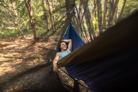 A smiling man lying comfortably in a Nakie hammock, with the Bug Net draped over, showcasing its effectiveness in providing insect protection for a blissful outdoor experience.