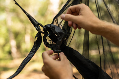 A person's hands attaching carabiners to Nakie's Bug Net, demonstrating the easy and secure setup process.