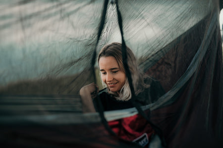 A woman enjoying her time in a Nakie hammock with a bug net, savoring the outdoor experience protected from insects.