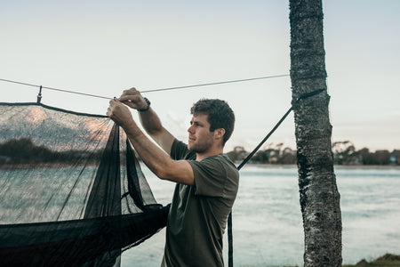 A man attaching guylines to Nakie's Bug Net, ensuring stability and security for outdoor use.