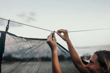 A smiling woman assembling guylines for Nakie's Bug Net, demonstrating ease of setup and preparation for insect-free outdoor relaxation.