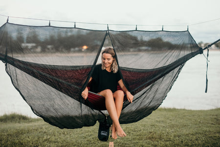 A woman relaxing in a Nakie hammock covered by our Bug Net, enjoying a peaceful outdoor experience protected from insects.