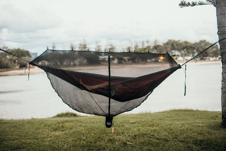 A woman relaxing inside Nakie's Bug Net while lying in a hammock, enjoying insect-free comfort during outdoor relaxation.