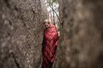 Image of a woman wrapped in Nakie's Earth Red Sustainable Down Puffy Blanket, enjoying warmth and sustainability during outdoor adventures. preview #7