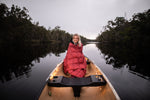 Image of a woman wrapped in Nakie's Earth Red Sustainable Down Puffy Blanket, sitting on a boat and enjoying warmth and sustainability during her maritime adventure. preview #2