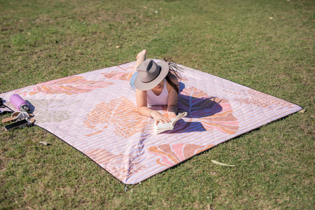 Image of a person enjoying a sunny picnic while reading, embodying relaxation and outdoor leisure with Nakie's eco-friendly products.