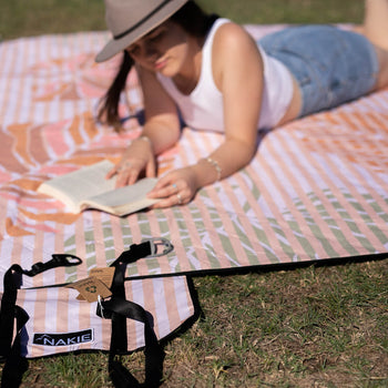 Woman enjoying a book at a Nakie picnic, surrounded by nature and relaxation, embodying the brand's commitment to outdoor leisure and sustainability.